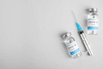 Vials with coronavirus vaccine and syringe on light background, flat lay. Space for text - obrazy, fototapety, plakaty