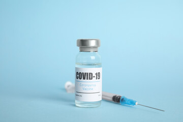 Vial with coronavirus vaccine and syringe on light blue background