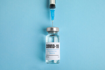 Filling syringe with coronavirus vaccine on light blue  background, flat lay