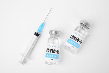 Vials with coronavirus vaccine and syringe on white background, flat lay