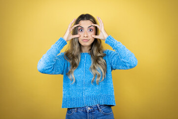Pretty blonde woman with long hair standing over yellow background Trying to open eyes with fingers, sleepy and tired for morning fatigue