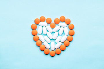 heart symbol formed orange pills or tablets isolated on a blue background. above view. outer space. cardiac medicine concept