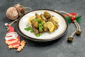 bottom view stuffed grape leaves on white plate and xmas pendants on dark background