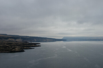 Obraz premium A beautiful foggy landscape in a blue-gray scale: a wide river, in front of the horizon are dark blue mountains, on the banks of the hills with dry grass. Colorado river, OR, USA