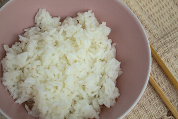Top view of pink bowl of cooked rice with bamboo hashi