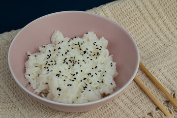 Top view of pink bowl of cooked rice decorated with black sesame