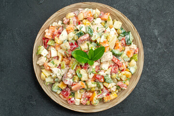 top close view of bowl of vegetable salad in the center with green on it on dark green background