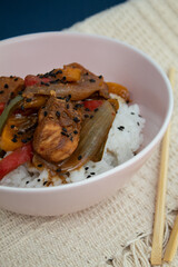 Closeup of bowl with cooked rice and plaid chicken decorated with black sesame with background
