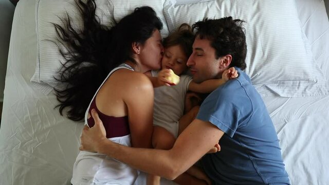 Parents hugging and kissing baby toddler in bed sharing love and affection