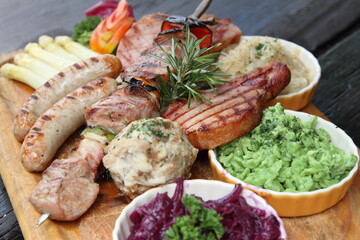 German mixed grill platter with sausages, pork chops, skewers, sauerkraut, asparagus, red cabbage, bread dumpling and wild garlic spätzle