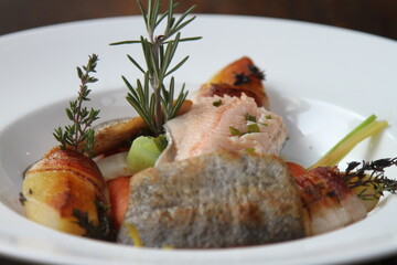 Austrian smoked trout fillets served with bacon wrapped boiled potatoes, root vegetables and rosemary, selective focus