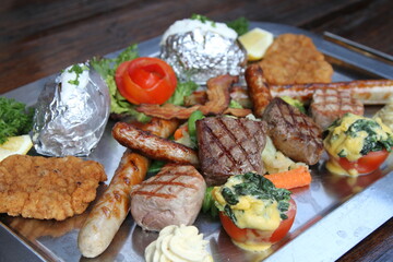 Huge mixed grill platter with crumbed pork escalope, beef steaks, pork steaks, German sausages, baked potatoes, herb butter and gratinated tomatoes