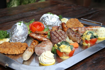 Huge mixed grill platter with crumbed pork escalope, beef steaks, pork steaks, German sausages, baked potatoes, herb butter and gratinated tomatoes