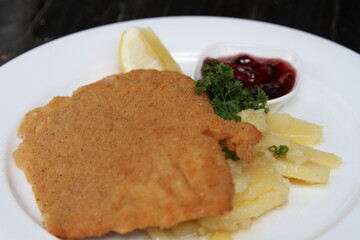 Crumbed pork escalope named Schnitzel, served with potato salad, cranberry jam and lemon