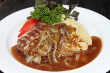 Pork steak with potato mash, onion jus and mixed greens