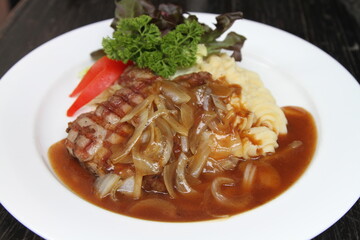 Pork steak with potato mash, onion jus and mixed greens