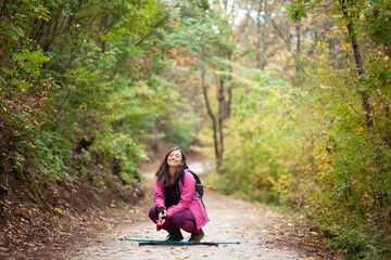 Hiker girl crouching on a trail in the mountains. Backpacker with pink jacket in a forest. Healthy fitness lifestyle outdoors.