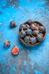 Vertical view of split and full fresh black mission figs in a small brown pot on blue background