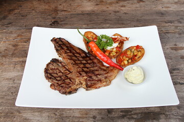 Grilled t-bone steak served with salsa filled potato skins, herb butter and chili