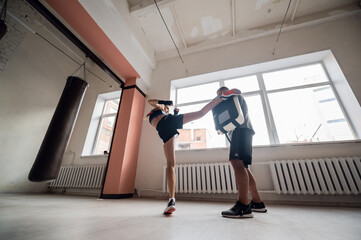 Fototapeta premium A young female athlete in good physical shape conducts kickboxing training under the supervision of an experienced male coach