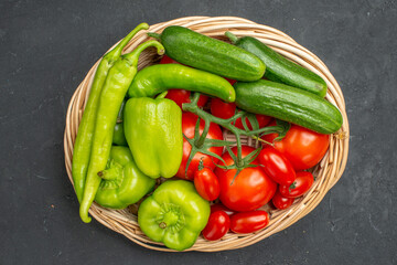 Fresh vegetables red tomatoes with stems green peppers and cucumbers necessary for cooking on dark background close up view