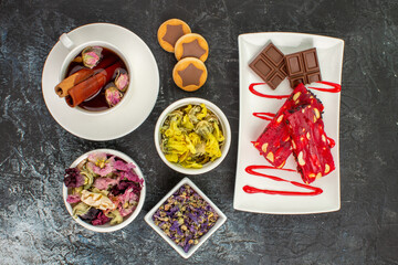 overhead view of herbal tea with chocolate on white plate with dry flowers on grey ground