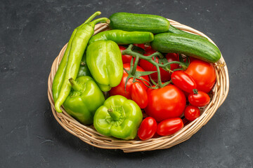 AFresh vegetablesred tomatoes with stems green peppers and cucumbers a bunch of green necessary for cooking on dark background