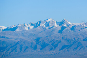 Low contrast photo of mountain range with snow peaks in different shades of blue and cyan. Flat contrast scene with negative space available for text. 