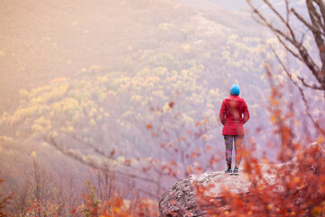 Hiking girl with poles and backpack standing on rocks. Windy autumn day. Travel and healthy...