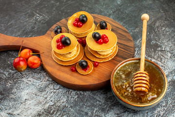 Close up view of fruit pancakes on wooden cutting board honey in a white bowl on gray background