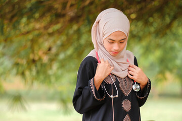 Young prethy Asean female doctor with hijab holding stethoscope in the hospital garden. Medical and healthcare doctor service concept.