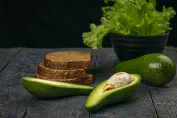 Avocado fruit and bread made from coarse flour on a black wooden table.