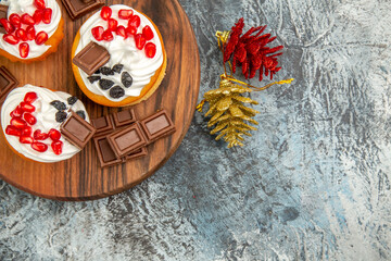 top close view berry cakes and chocolates on chopping board golden and red pinecones on grey-white background with copy space