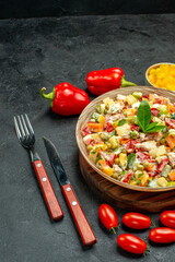 side close view of bowl of vegetable salad with fork and knife and vegetables on side with free place for your text on dark grey table