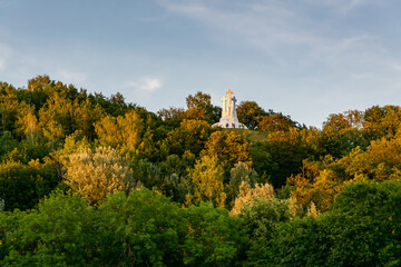 Vilnius, Lithuania - 07.25.2020: Mountain of Three Crosses, white monument on top of the mountain, around yellow orange and green trees, blue sky, summer daytime.