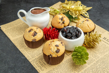 Front close view of small cupcakes chocolates black raisin and accessories on newspaper on dark isolated background