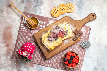 top view raisin cake slices with raspberries on cutting board bowl with raspberry candies biscuits honeycomp stick in honey bowl xmas toy a newspaper on marble ground