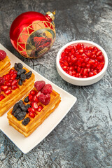 top view waffles with berries on white plate red xmas tree ball bowl with pomegranates on grey-white background