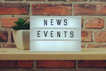 News Events word in light box on brick wall and wooden shelves background