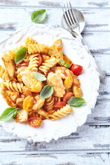Pasta with chicken breast, cherry tomatoes and fresh basil. Bright wooden background. Top view.