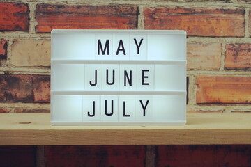 May, June, July word in light box on wooden shelves background