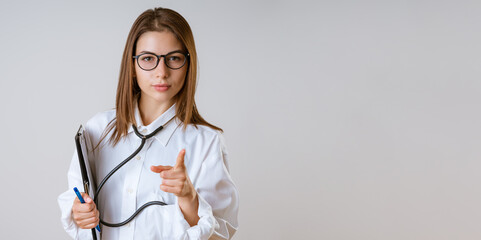 Young woman doctor points a finger, isolated on gray background.