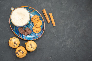 Top view of delicious breakfast with a cup of milk various biscuits and chocolate bars on dark...