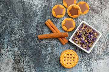 close up view of cinnamon sticks with a bowl of dry flower and cookies on grey background