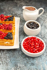 bottom view waffles with berries on rectangular plate bowls with pomegranates raisins hot chocolate on grey-white background