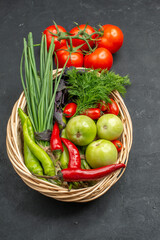 A vegetable basket with a bunch of green and peppers cucumber and tomatoes with stem on dark background