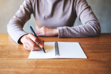 Closeup image of a woman writing on a blank notebook on the table