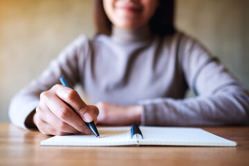 Closeup image of a woman writing on a blank notebook on the table