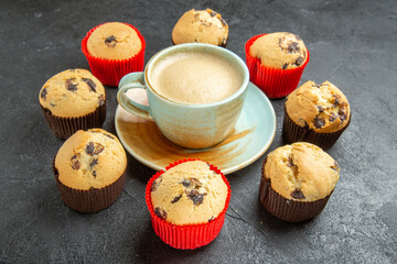 Front close view of delicious coffee around small cupcakes on dark background
