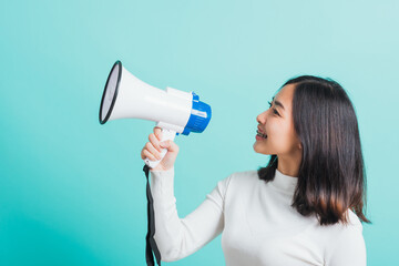 Beautiful Asian woman smile she holding megaphone making the announcement, female excited cheerful announce good news isolated on a blue background